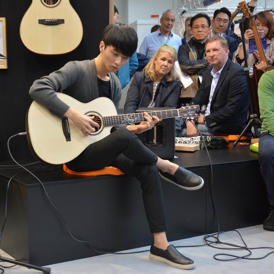 Sungha Jung performing at Musikmesse on his signature acoustic guitar at MusikMesse with people looking at him and being very interested.