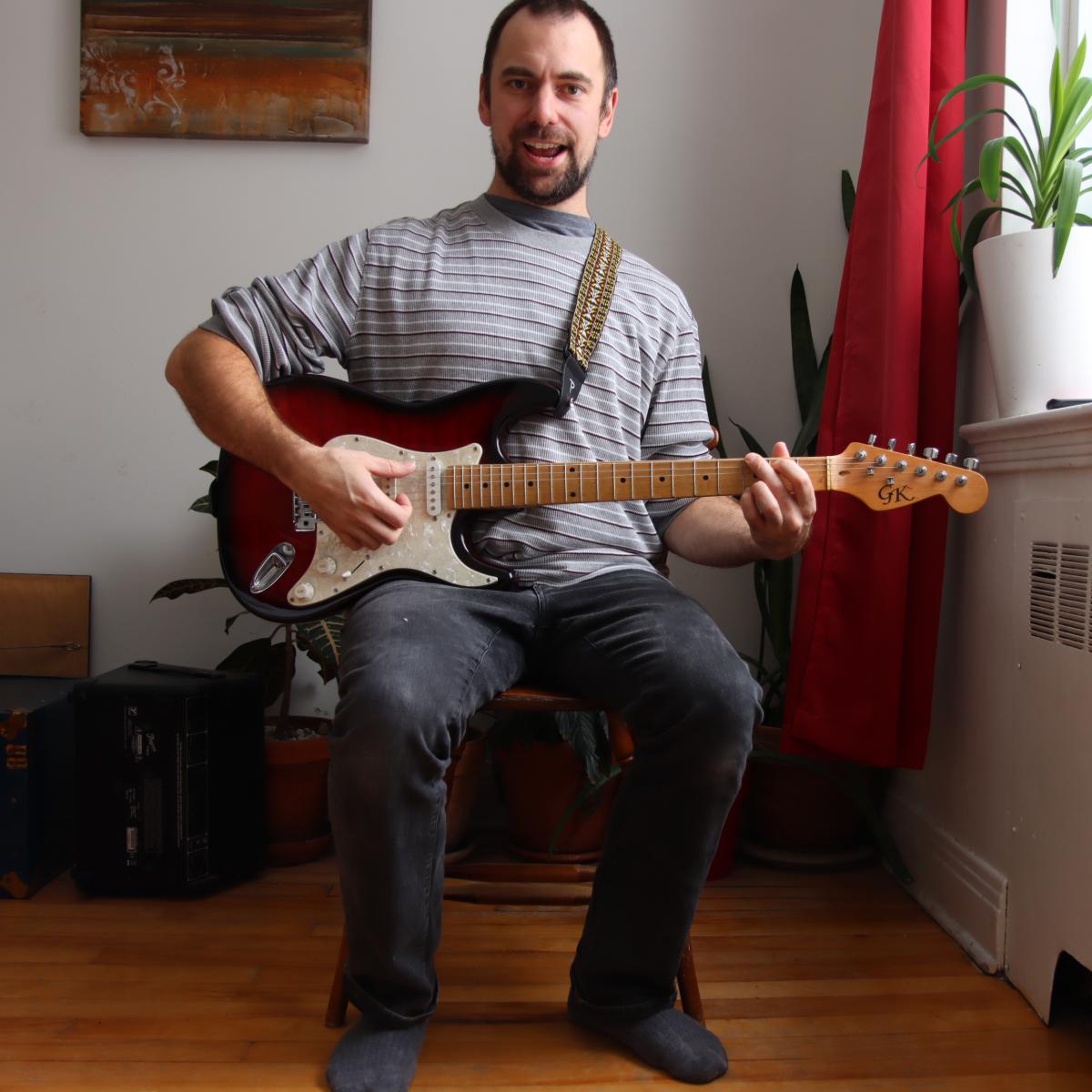 Brett holding an electric guitar and smiling as he plays these awesome warm up exercises