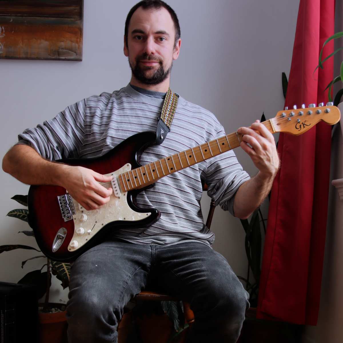 Brett holding an electric guitar and smiling as he places a chord