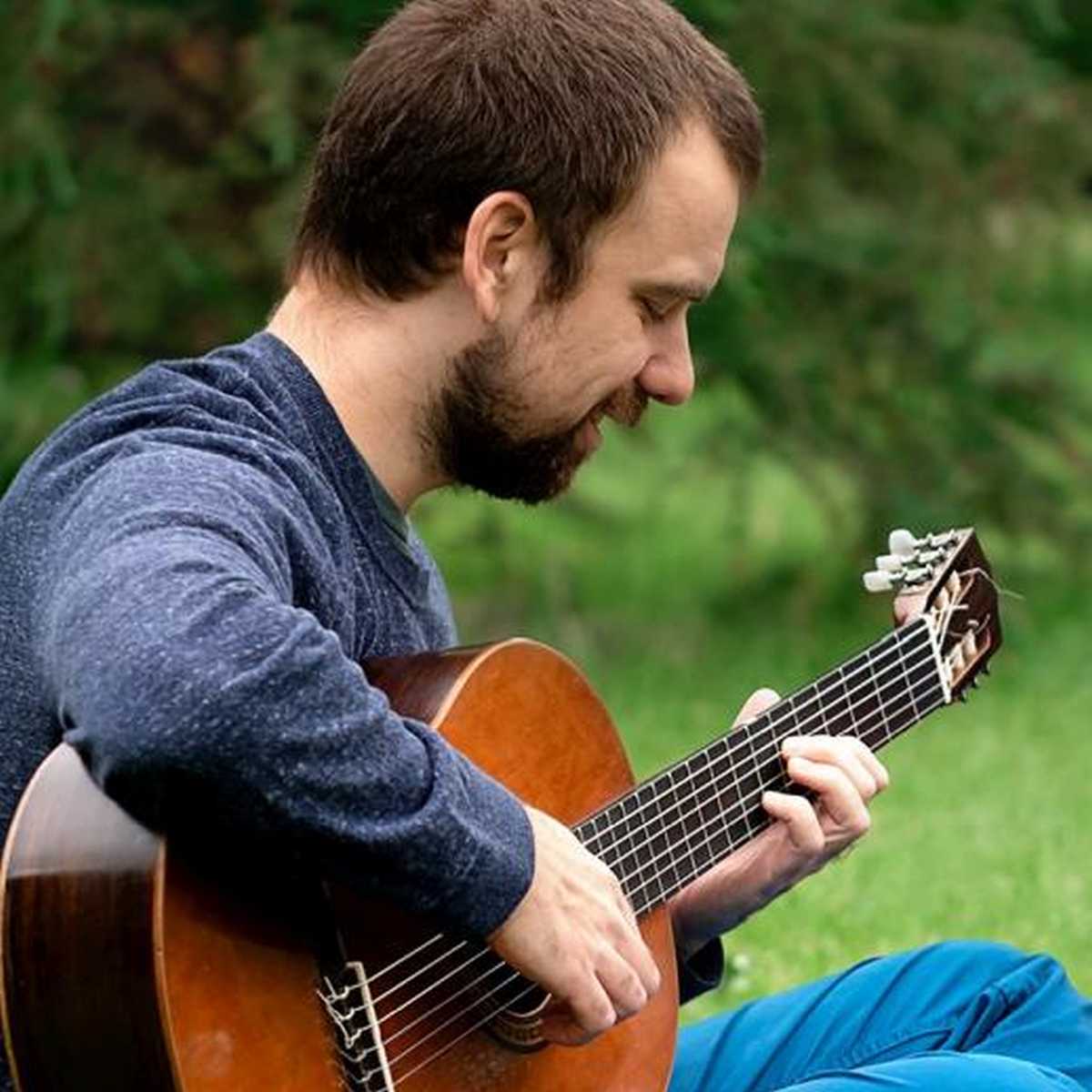 Brett playing fingerstyle guitar while sitting on the grass in a park