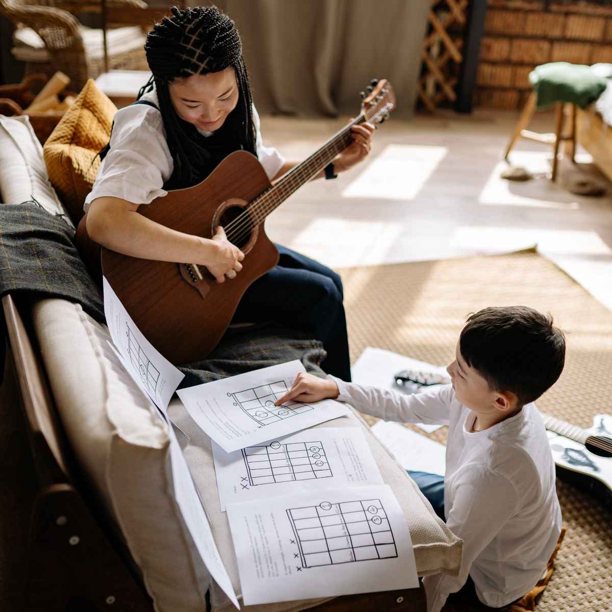 A girl playing guitar and a boy pointing at a fretboard diagram, both participating in an effective guitar practice session.