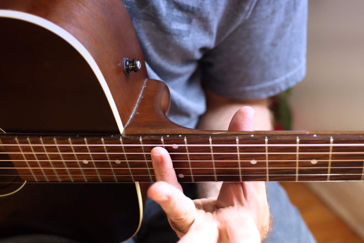 An image of the finger placed at the twelfth fret to produce a guitar harmonic